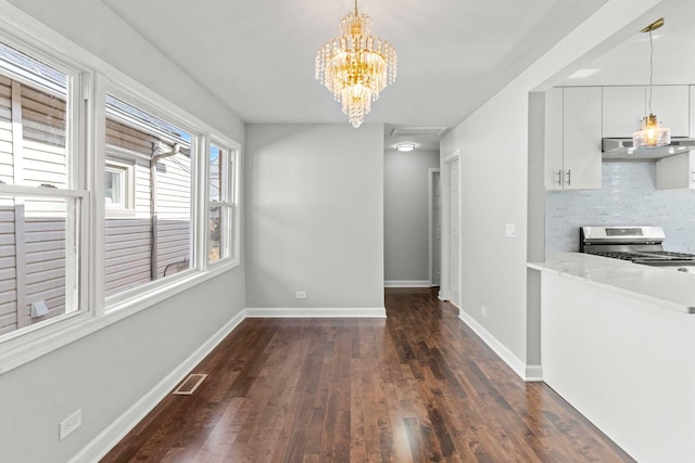 unfurnished dining area with dark wood-style floors, visible vents, an inviting chandelier, and baseboards