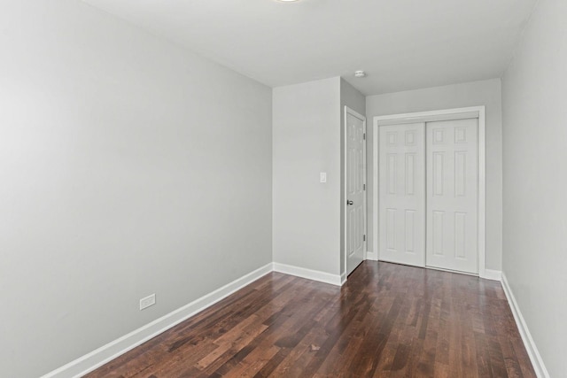 unfurnished bedroom with baseboards, dark wood-style flooring, and a closet