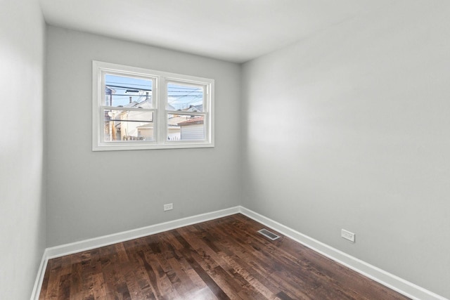 spare room featuring dark wood-style flooring, visible vents, and baseboards