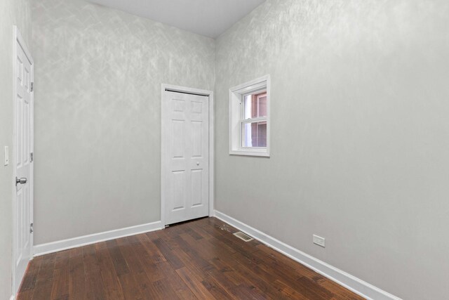 empty room featuring visible vents, dark wood-style floors, and baseboards