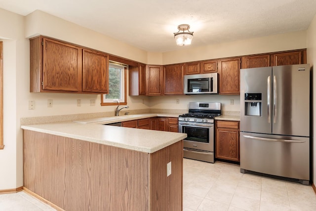 kitchen with a peninsula, light countertops, appliances with stainless steel finishes, and brown cabinets