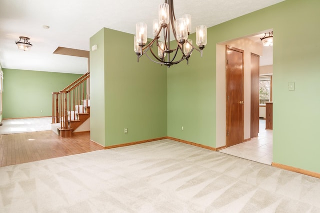 carpeted spare room with baseboards, a notable chandelier, and stairs