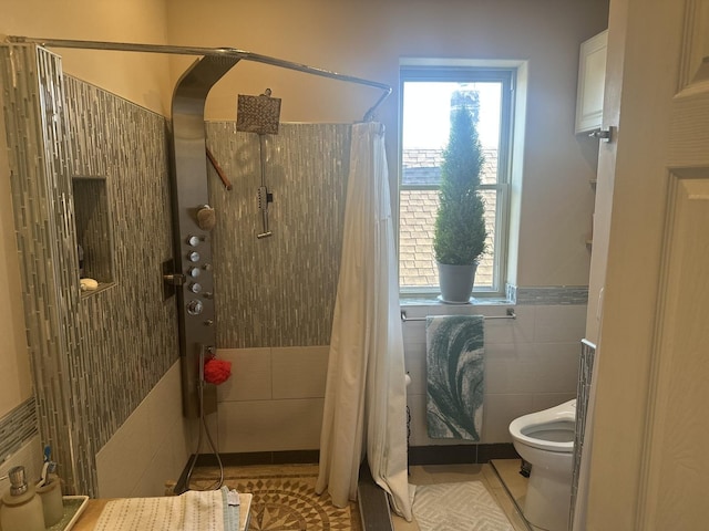 full bath with tiled shower, tile patterned flooring, toilet, wainscoting, and tile walls