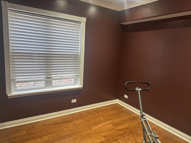 empty room featuring crown molding, baseboards, and wood finished floors