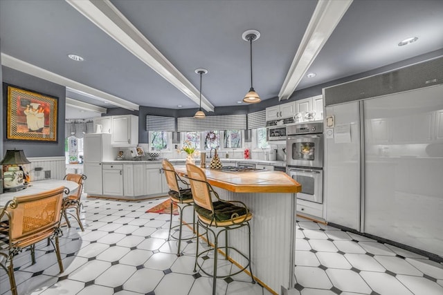 kitchen featuring appliances with stainless steel finishes, a kitchen bar, beam ceiling, and light floors