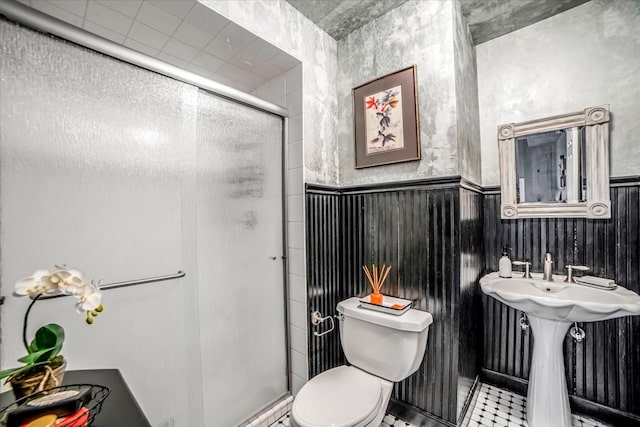bathroom with a sink, wainscoting, toilet, and a shower stall