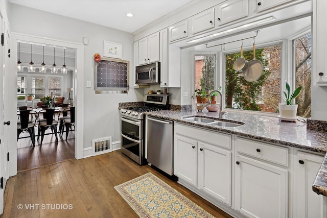 kitchen featuring stainless steel appliances, a sink, baseboards, visible vents, and white cabinetry