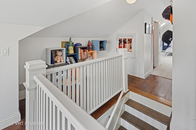 stairs with wood finished floors, lofted ceiling, and baseboards