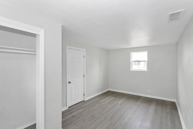 unfurnished bedroom featuring visible vents, baseboards, a closet, and wood finished floors