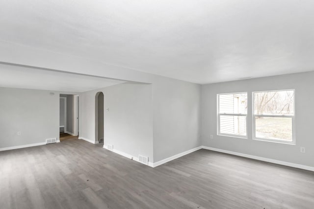 empty room featuring visible vents, baseboards, arched walkways, and wood finished floors