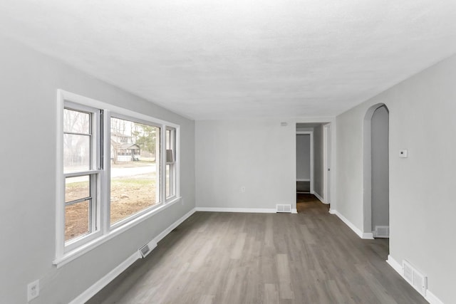 spare room with arched walkways, visible vents, dark wood-style flooring, and baseboards