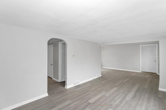 unfurnished room with arched walkways, visible vents, baseboards, and wood finished floors
