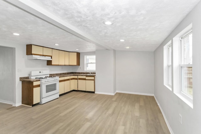 kitchen with a sink, light wood-type flooring, dark countertops, under cabinet range hood, and white gas range oven