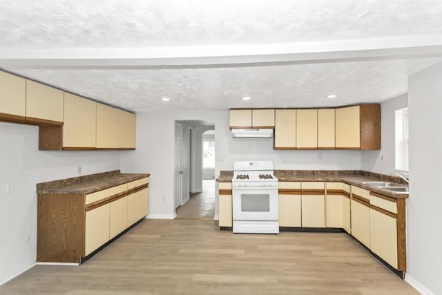 kitchen with a sink, gas range gas stove, under cabinet range hood, cream cabinetry, and beamed ceiling