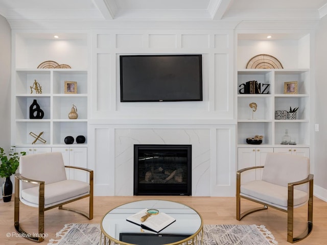 living room featuring light wood-style flooring, a fireplace, ornamental molding, and built in shelves