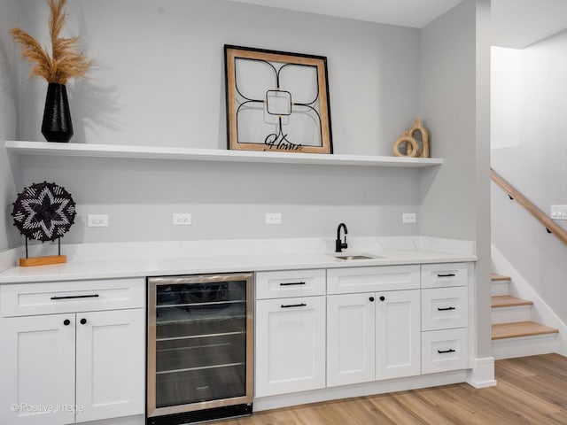 bar with a sink, bar area, stairs, light wood-style flooring, and beverage cooler