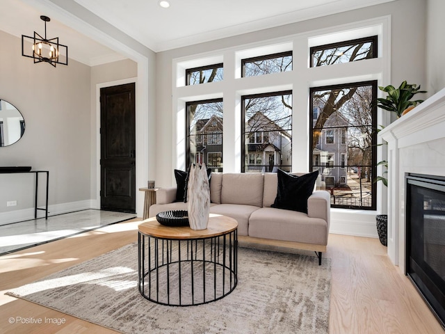living room with baseboards, a notable chandelier, ornamental molding, light wood-style floors, and a premium fireplace