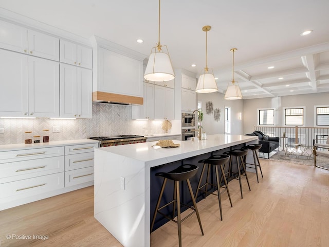 kitchen featuring tasteful backsplash, an island with sink, a breakfast bar, white cabinetry, and light wood-style flooring