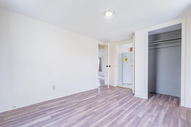 unfurnished bedroom featuring light wood-style flooring, a closet, freestanding refrigerator, and baseboards