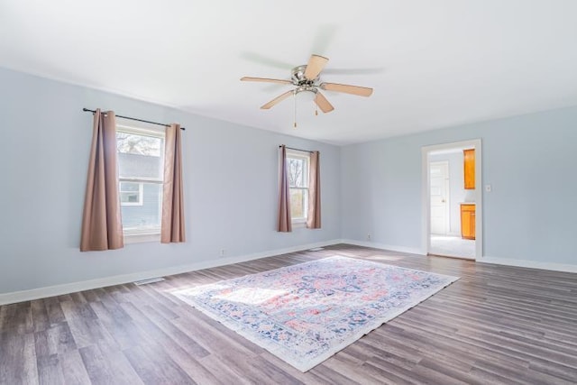 spare room with ceiling fan, plenty of natural light, wood finished floors, and baseboards