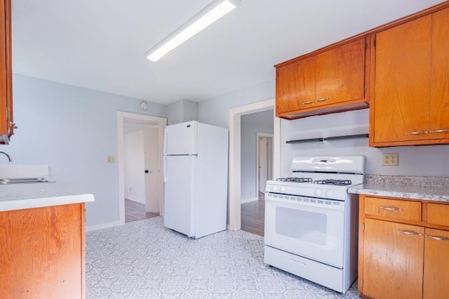 kitchen with brown cabinetry, a sink, light countertops, and white appliances