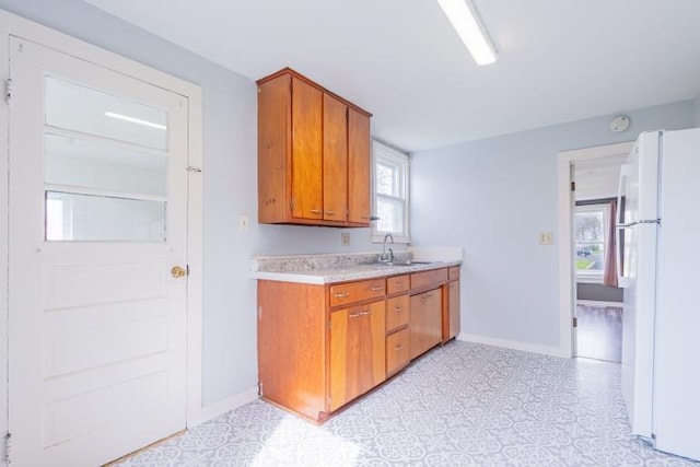 kitchen with freestanding refrigerator, light countertops, a sink, brown cabinets, and baseboards