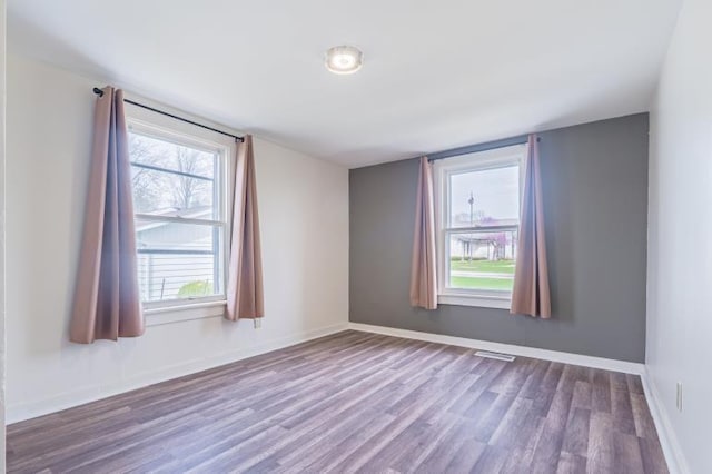 spare room with plenty of natural light, visible vents, baseboards, and wood finished floors