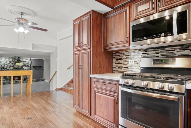 kitchen with light wood-style flooring, light countertops, backsplash, a ceiling fan, and appliances with stainless steel finishes
