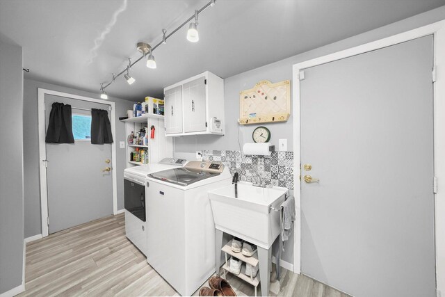 clothes washing area with rail lighting, washing machine and dryer, light wood-style flooring, and cabinet space
