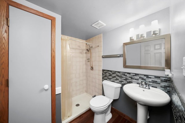 full bath featuring a tile shower, visible vents, toilet, wood finished floors, and a sink