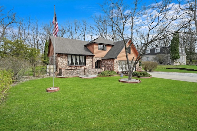 tudor home with a front yard, a shingled roof, brick siding, and driveway