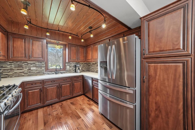 kitchen with track lighting, light wood-style flooring, light countertops, decorative backsplash, and appliances with stainless steel finishes