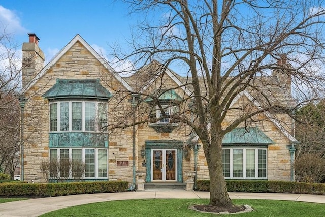 english style home with french doors, a front yard, stone siding, and a chimney