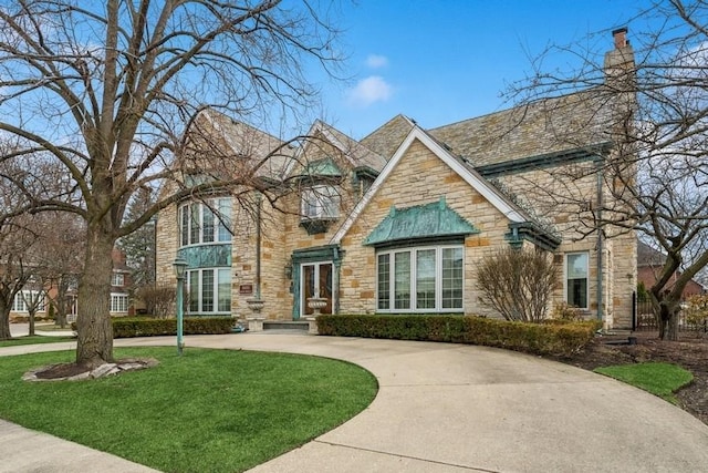 view of front of property featuring curved driveway, a chimney, stone siding, and a front lawn