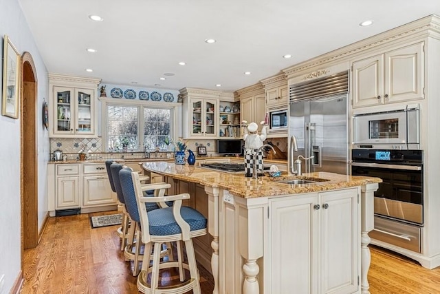 kitchen featuring built in appliances, light wood-style flooring, light stone counters, and cream cabinetry