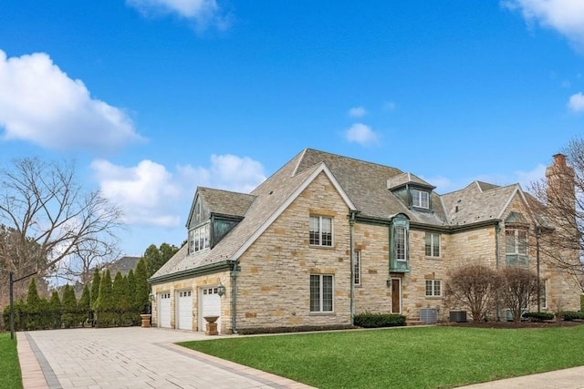view of front of house with central air condition unit, a front yard, stone siding, an attached garage, and driveway