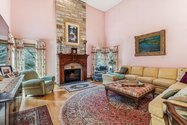 living room with a wealth of natural light, wood finished floors, a high ceiling, and a glass covered fireplace