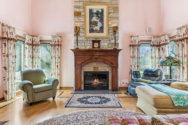 sitting room with wood finished floors, a towering ceiling, a glass covered fireplace, and baseboards