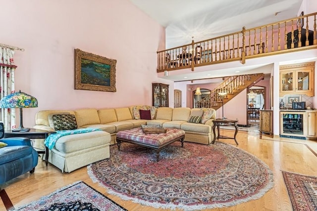 living area featuring a high ceiling, beverage cooler, wood finished floors, and stairs