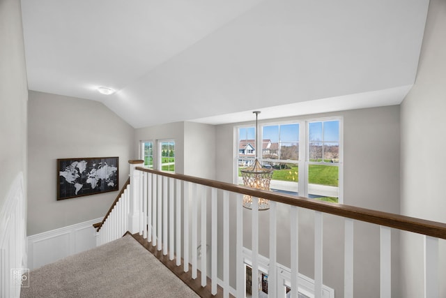 hall with an inviting chandelier, an upstairs landing, a wainscoted wall, lofted ceiling, and a decorative wall