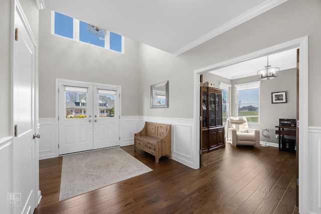 foyer with a chandelier, ornamental molding, dark wood-style floors, and a wainscoted wall