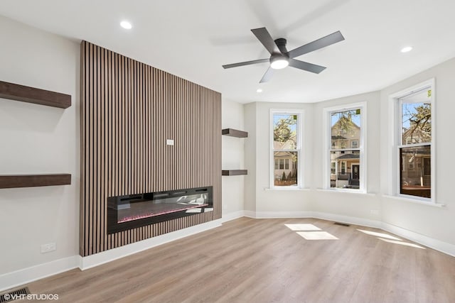 unfurnished living room featuring recessed lighting, ceiling fan, a glass covered fireplace, and wood finished floors