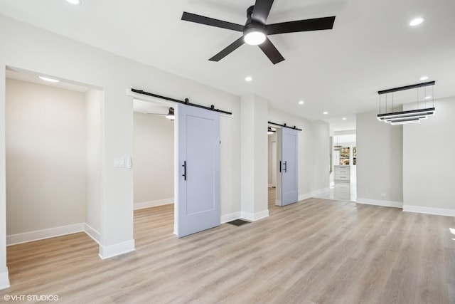 unfurnished living room with light wood-type flooring, a barn door, a ceiling fan, and recessed lighting