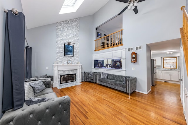 living area with high vaulted ceiling, light wood-style floors, visible vents, and a fireplace