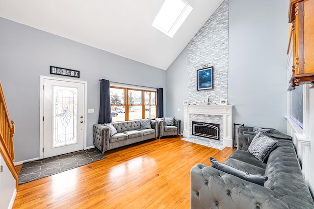 living room featuring wood finished floors, a stone fireplace, a skylight, baseboards, and high vaulted ceiling