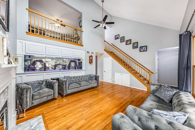 living room with a fireplace with flush hearth, light wood finished floors, a ceiling fan, stairs, and high vaulted ceiling