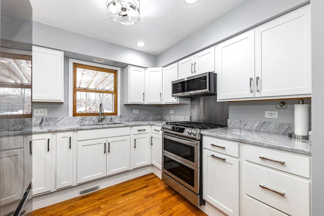 kitchen featuring white cabinets, stainless steel appliances, visible vents, a sink, and light stone countertops