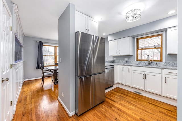 kitchen with light stone counters, a sink, light wood-type flooring, white cabinets, and appliances with stainless steel finishes