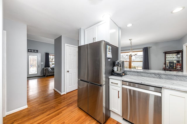 kitchen featuring white cabinets, light wood-type flooring, an inviting chandelier, light stone counters, and appliances with stainless steel finishes