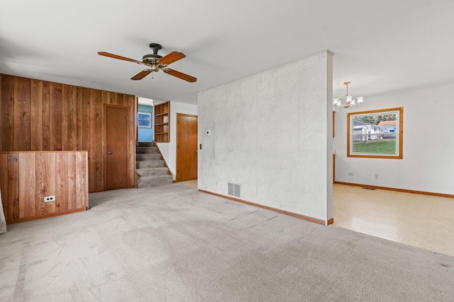 unfurnished room featuring stairway, ceiling fan with notable chandelier, carpet, wood walls, and visible vents